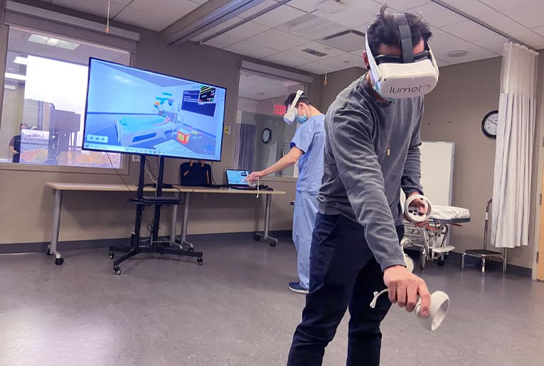Two learners running InvolveXR on Lumeto VR headsets in a nursing sim lab, the scenario displayed on a monitor beside them