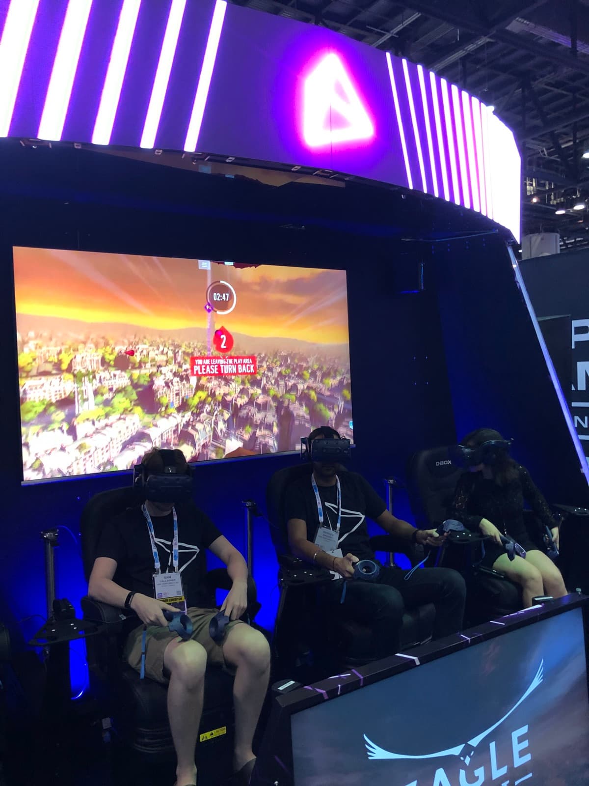 The Vusr Stage attraction mid-session: Eagle Flight gameplay on the display while three players ride synced D-BOX motion chairs beneath the booth's LED arch